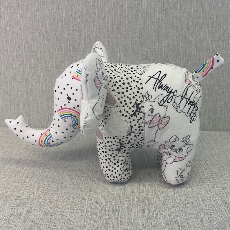 May include: A white and black patchwork elephant plush toy with a rainbow design on the trunk. The elephant has a black and white polka dot pattern on one side and a white background with a black and white cat illustration and the text "Always Happy" on the other side.