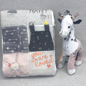 Peut inclure: Une courtepointe bébé en patchwork avec un motif gris, rose et blanc. La courtepointe présente une variété de motifs, notamment des flèches, un lapin et les mots "you are loved". Un jouet en peluche en forme de girafe est également représenté.