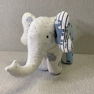 May include: A white stuffed elephant toy with blue star print fabric. The elephant has a blue and white striped ear with the text "big smiles all day".