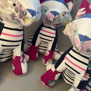 May include: Three plush toys shaped like foxes, each with a different floral pattern on their bodies. The foxes are made of a patchwork of fabrics, including blue and white striped fabric, pink and white striped fabric, and floral fabric. The foxes are sitting on a gray surface.