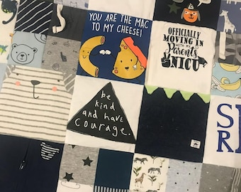 May include: A patchwork quilt made from baby clothes. The quilt is composed of squares in various colours and patterns, including shirts with text such as "two peas in a pod" and "be kind and have courage."