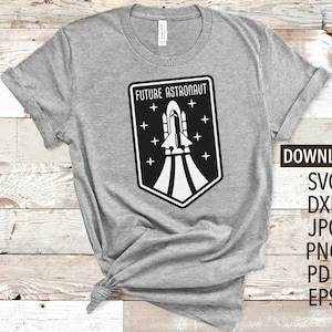 May include: A gray t-shirt with a black and white graphic of a rocket ship and the text "Future Astronaut".