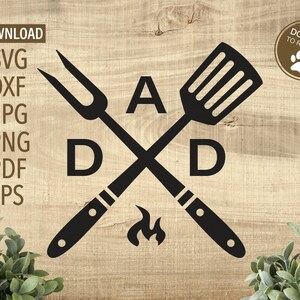 Może przedstawiać: Czarno-biały projekt graficzny z łopatką i widelcem do grillowania skrzyżowanymi ze sobą z literami "DAD" i "A" w środku. Projekt jest na drewnianym tle.