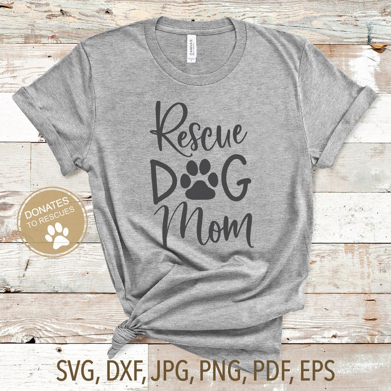 Pu&ograve; includere: Maglietta grigia con il testo "Rescue Dog Mom" e una grafica di impronta di zampa. Il testo "Donates to Rescues" &egrave; in un cerchio con una grafica di impronta di zampa.