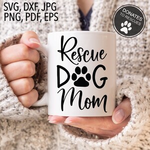 Pu&ograve; includere: Una tazza in ceramica bianca con testo nero che recita "Rescue Dog Mom" e un'impronta di zampa. La tazza &egrave; tenuta da una persona che indossa un maglione bianco.