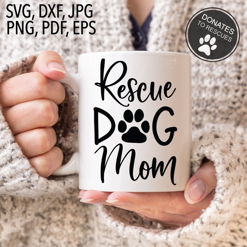 Pu&ograve; includere: Una tazza in ceramica bianca con testo nero che recita "Rescue Dog Mom" e un'impronta di zampa. La tazza &egrave; tenuta da una persona che indossa un maglione bianco.