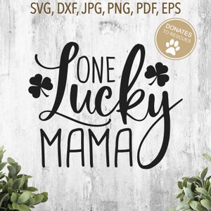 Op de afbeelding: Zwart-wit grafisch ontwerp met de tekst "One Lucky Mama" en twee klavertjesvier designs. De grafiek is op een witte houten achtergrond.