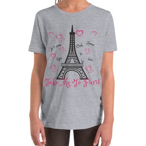 K&ouml;nnte beinhalten: Ein graues T-Shirt f&uuml;r Jugendliche mit einem schwarz-wei&szlig;en Motiv des Eiffelturms und dem Text "Take Me To Paris". Das Motiv enth&auml;lt auch rosa Herzen und die franz&ouml;sischen S&auml;tze "Je t'aime", "Oh la la", "Bisous" und "Amour".