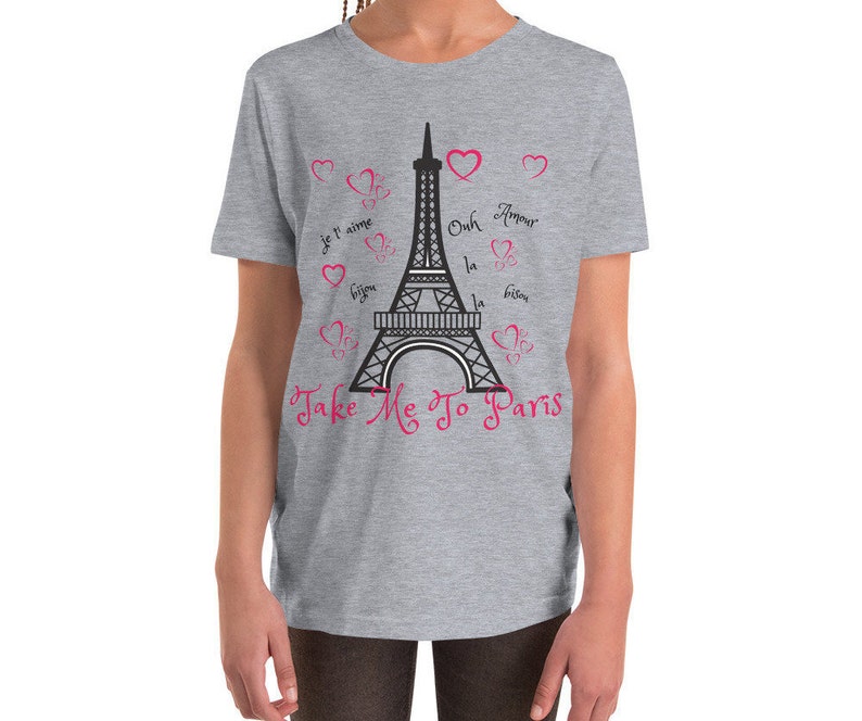 K&ouml;nnte beinhalten: Ein graues T-Shirt f&uuml;r Jugendliche mit einem schwarz-wei&szlig;en Motiv des Eiffelturms und dem Text "Take Me To Paris". Das Motiv enth&auml;lt auch rosa Herzen und die franz&ouml;sischen S&auml;tze "Je t'aime", "Oh la la", "Bisous" und "Amour".