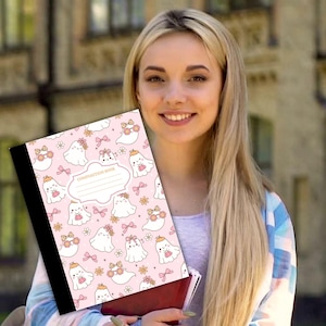 May include: A pink composition book featuring a pattern of adorable ghost characters adorned with bows and floral crowns. The cover includes the text "COMPOSITION BOOK" and a blank label. The book has a black spine.