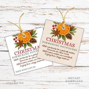以下が含まれることがあります： オレンジスライス、シナモンスティック、松ぼっくりが付いた2つのクリスマスのポプリタグ。「Christmas Simmering Potpourri」のテキストと説明が記載されています。1つのタグは白、もう1つはベージュです。