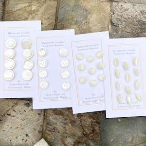 Könnte beinhalten: Vier Karten mit weißen Keramikknöpfen. Jede Karte zeigt einen anderen Knopfstil und enthält den Text "Handmade Ceramic Stoneware Buttons" und "By Duska Martovich Scarborough, Maine".