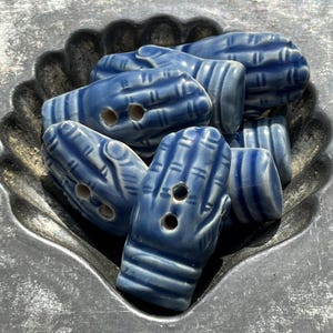 May include: A collection of blue ceramic buttons shaped like hands, each featuring two holes for attachment. The buttons have a glossy finish with darker blue detailing that highlights the finger and wrist contours, creating a uniform appearance.