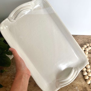 May include: A white ceramic serving tray with two handles on either side. The tray is rectangular and has a slightly raised edge.