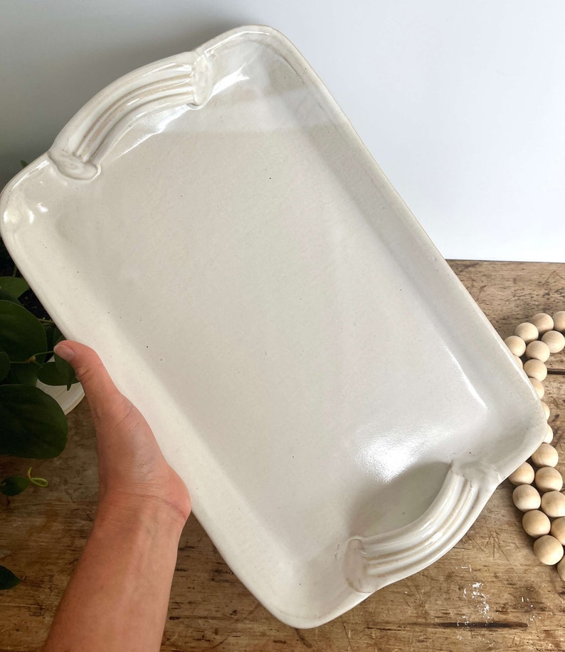 May include: A white ceramic serving tray with two handles on either side. The tray is rectangular and has a slightly raised edge.
