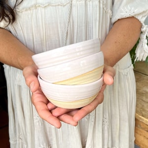 May include: Three stacked ceramic bowls with a light pink glaze and a thin beige stripe around the rim.