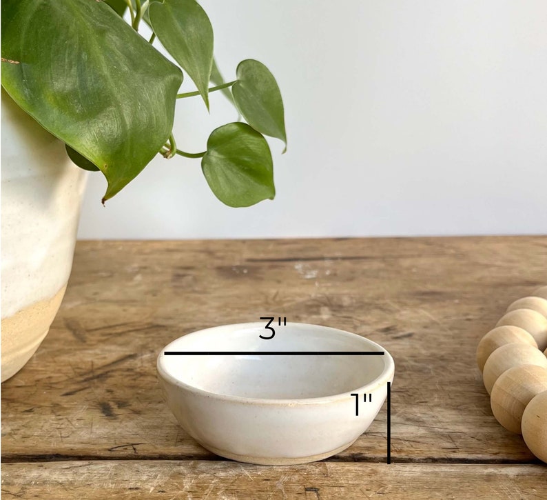 May include: A small white ceramic bowl with a 3-inch diameter and 1-inch height. The bowl is sitting on a wooden surface.