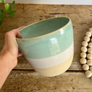 May include: A large, ceramic planter with a light green glaze on the top, a white glaze in the middle, and a light brown glaze on the bottom.