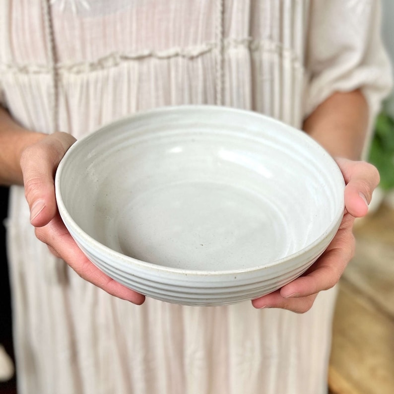 May include: A white ceramic bowl with a slightly textured, rippled surface. The bowl is empty and appears to be handmade.