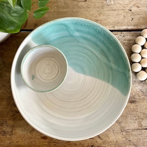 May include: A white ceramic serving dish with a smaller bowl attached. The dish is glazed in a light green colour on one side and white on the other.
