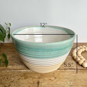 May include: A large, white ceramic bowl with a light blue and beige glaze. The bowl is 12 inches wide and 5.5 inches tall.
