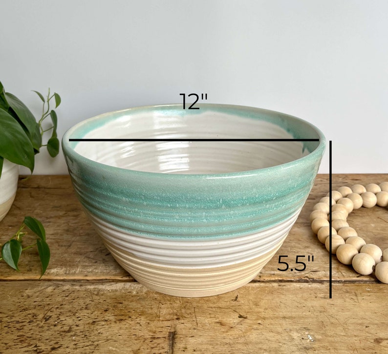 May include: A large, white ceramic bowl with a light blue and beige glaze. The bowl is 12 inches wide and 5.5 inches tall.
