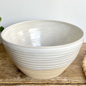 May include: A large white ceramic bowl with a cream-coloured rim. The bowl has a textured, ribbed design.