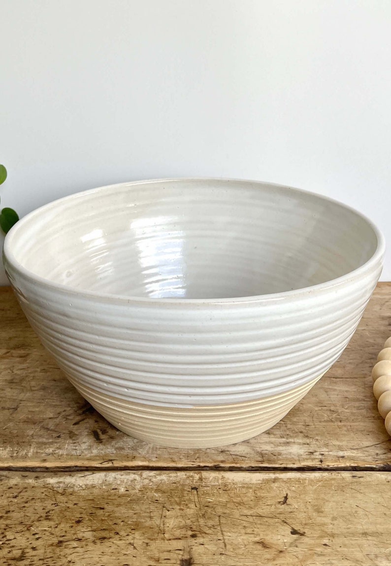 May include: A large white ceramic bowl with a cream-coloured rim. The bowl has a textured, ribbed design.