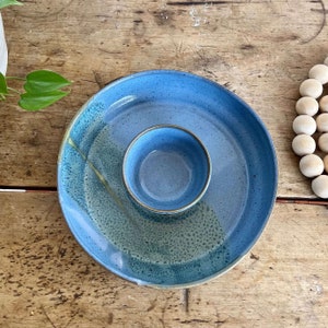 May include: A blue ceramic serving dish with a smaller bowl in the center. The dish has a speckled glaze and a light blue color.
