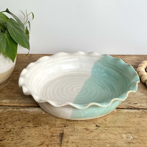 May include: A white and light blue ceramic pie plate with a fluted edge. The plate is glazed in a white and light blue color scheme.