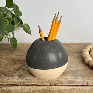 May include: A black and white ceramic pencil holder with a rounded shape. The holder has a dark gray top and a light beige bottom. It is filled with yellow pencils.