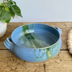 May include: A blue and green ceramic baking dish with two handles. The dish has a speckled glaze and a striped design.