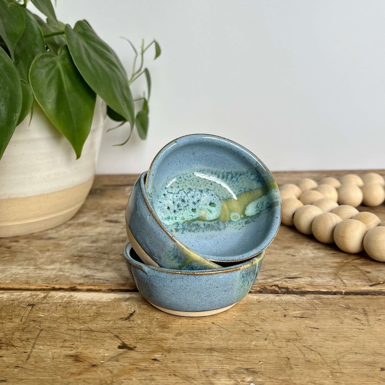 May include: Three small blue ceramic bowls with a green and white glaze. The bowls are stacked on top of each other.