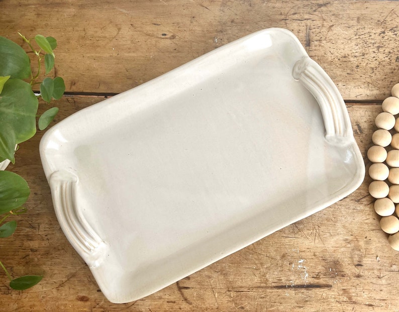 May include: A white ceramic serving tray with two handles. The tray is rectangular and has a smooth, glossy finish.