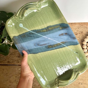 May include: A green ceramic serving tray with blue and brown accents and two handles. The tray has a glossy finish.