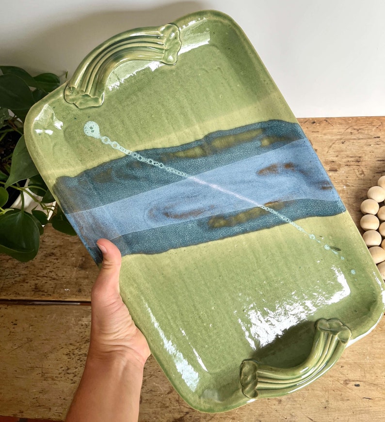 May include: A green ceramic serving tray with blue and brown accents and two handles. The tray has a glossy finish.