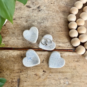 May include: Four small heart-shaped ceramic dishes in a light blue and white speckled glaze. Two of the dishes have rings inside.