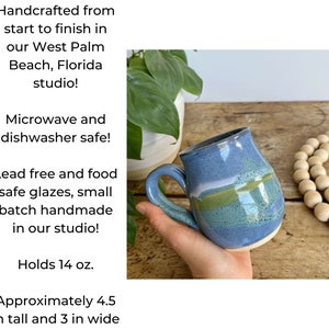 Op de afbeelding: Een handgemaakte keramische mok met een blauwe glazuur en groene en witte strepen. Hij heeft een inhoud van 14 ounce en is ongeveer 4,5 inch hoog en 3 inch breed. Geschikt voor magnetron en vaatwasser.