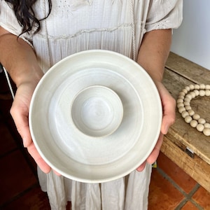 May include: A white ceramic serving dish with a smaller bowl in the center. The dish has a slightly textured surface and a simple, modern design.