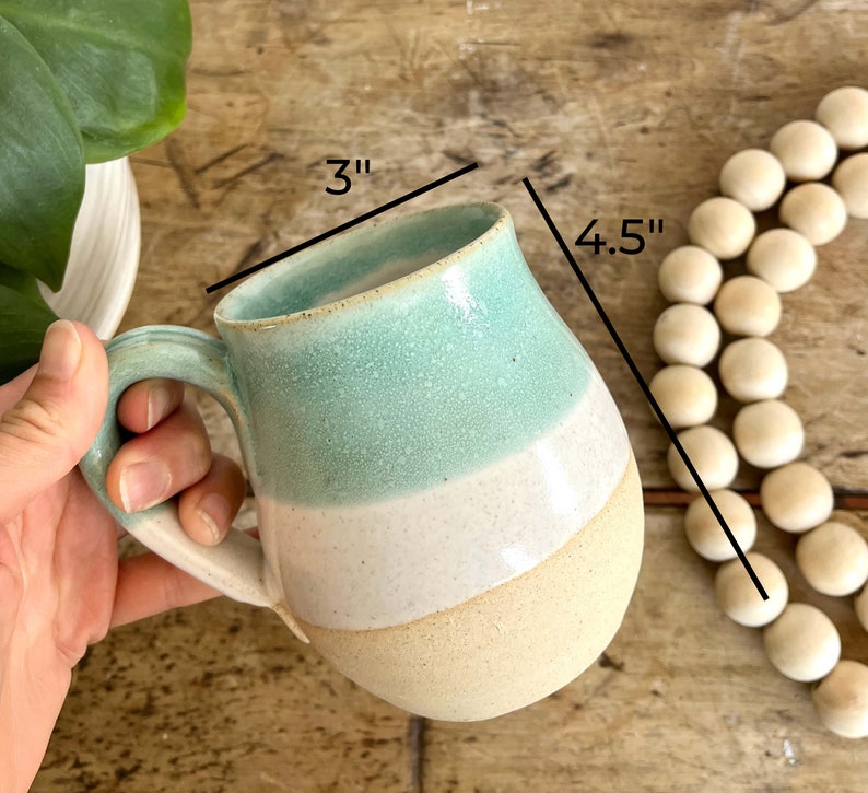 May include: A light blue, white, and beige ceramic mug with a handle. The mug is 4.5 inches tall and 3 inches wide.