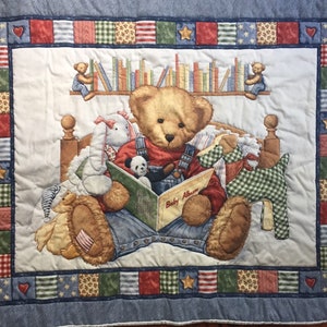May include: A patchwork quilt with a blue denim border features a teddy bear reading a book titled "Baby Album". The bear is surrounded by other stuffed animals, including a bunny, a panda, and a dog. The quilt has a bookshelf with books above the bear and a red, white, and blue border.