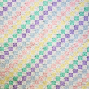 May include: A patchwork quilt with a checkered pattern in shades of pink, yellow, light blue, purple, and green.