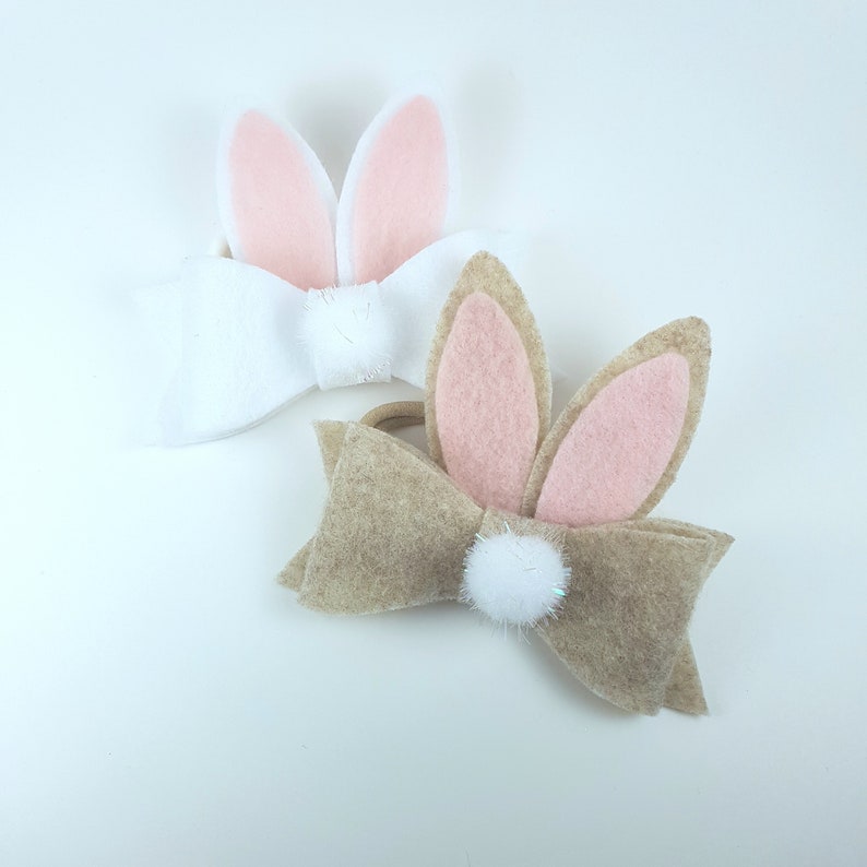 May include: Two felt bunny hair bows with white pom poms. One bow is white with pink ears and the other is brown with pink ears.