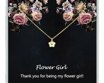 May include: A gold flower necklace with a pink center stone in a black box with a floral design and the text "Flower Girl" and "Thank you for being my flower girl!"