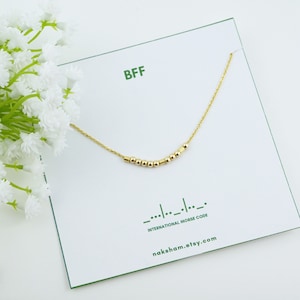 May include: Gold necklace with a chain and small beads spelling out "BFF" in international Morse code. The necklace is displayed on a white card with the text "BFF", "INTERNATIONAL MORSE CODE", and "naksham.etsy.com".