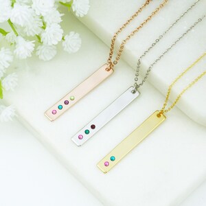 May include: Three bar necklaces with different colored gemstones. The necklaces are rose gold, silver, and gold. Each necklace has a bar pendant with three gemstones.