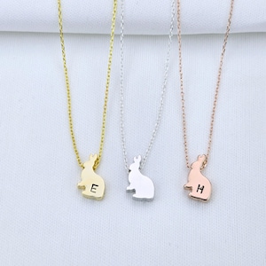 May include: Three delicate necklaces with bunny pendants. The bunny pendants are gold, silver, and rose gold. Each pendant has a letter engraved on it: E, H, and a third letter that is not visible in the image.