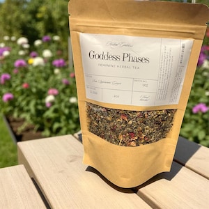 May include: A brown paper bag of "Goddess Phases" feminine herbal tea. The bag has a clear window showing the tea blend of herbs and flowers. The label reads "Pure Peppermint Ginger" and the bag contains 2 oz of tea.