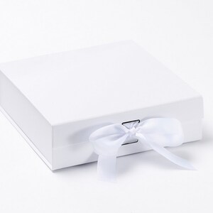 May include: A white, square gift box with a matching white satin ribbon tied in a bow. The box is closed and has a magnetic closure. The box is on a white background.