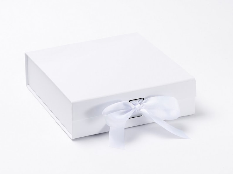 May include: A white, square gift box with a matching white satin ribbon tied in a bow. The box is closed and has a magnetic closure. The box is on a white background.